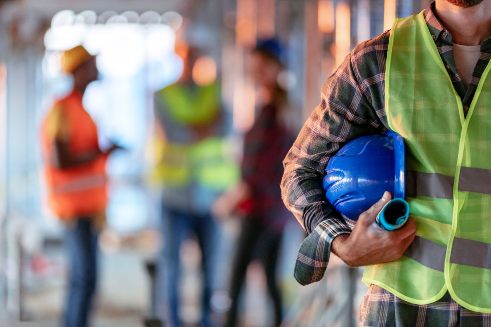 Homme tenant un casque bleu, gros plan. Homme travaillant dans la construction avec un bureau et des gens en arrière-plan. Gros plan de la main d'un ouvrier de la construction tenant un casque de travail.
