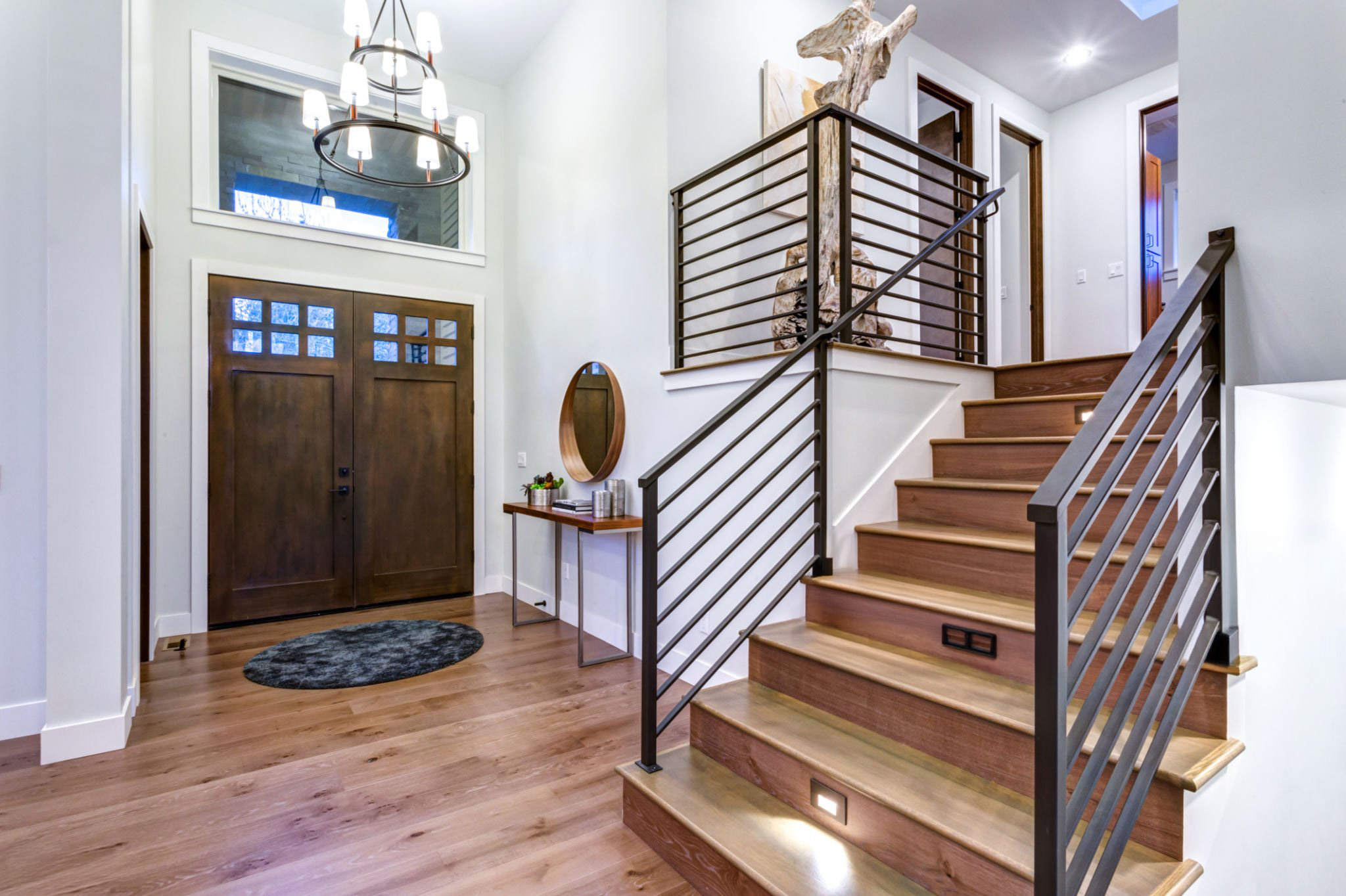 Entrée chic avec un haut plafond et un large escalier avec des lumières et une rampe contemporaine. Intérieur d'une nouvelle maison construite sur mesure.