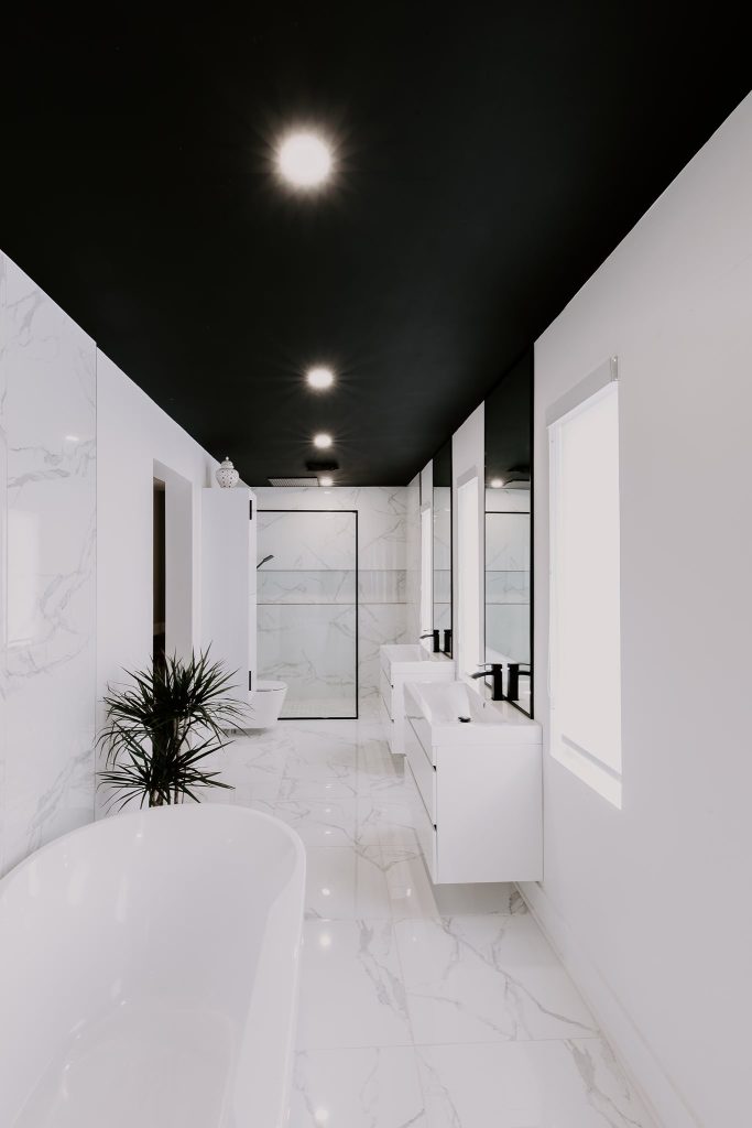 Salle de bain moderne avec des murs et un sol en marbre blanc, plafond noir, baignoire indépendante, et douche vitrée.