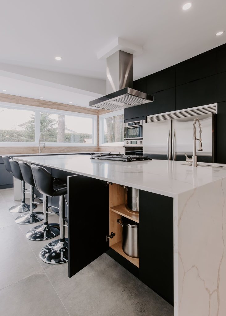 Cuisine moderne avec un îlot central en marbre blanc, des armoires noires, des tabourets en cuir noir, et des appareils en acier inoxydable.