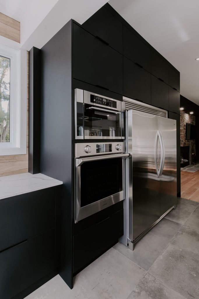 Cuisine moderne avec des armoires noires, un four encastré en acier inoxydable, et un réfrigérateur double porte assorti.